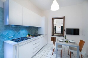 Eine moderne Küche mit weißen Schränken, einer blauen Spritzschutzwand, einem Gasherd und einem Essbereich mit Tisch und Stühlen.