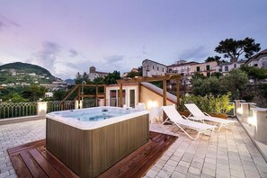Eine Dachterrasse mit Whirlpool, Liegestühlen und Blick auf eine Hügelstadt.
