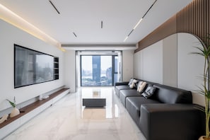 A modern living room with a large flat-screen TV, a black leather sofa, a coffee table, and a large window with a city view. - Zhome- Three Bedrooms Super Bund View (Shanghai)