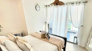Een slaapkamer met een bed, nachtkastje, klok en raam met gordijnen.