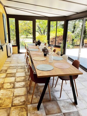 A long dining table with chairs, a ceiling fan, and large windows with a garden view. - Stunning Villa—Extra-Large Pool—Air Conditioning—Fireplace—Large Garden (Gaillac)