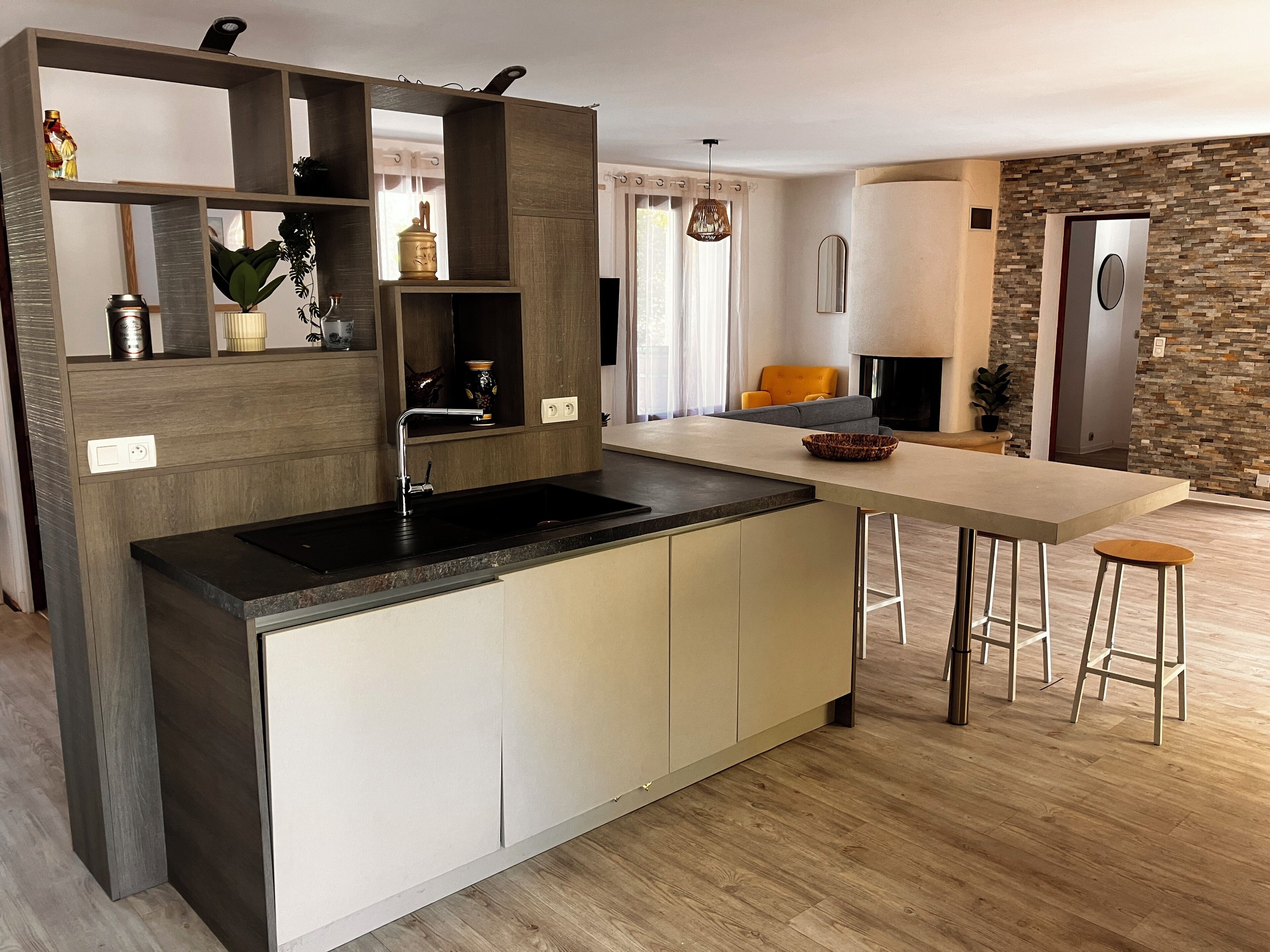 Une cuisine moderne dotée d’un îlot central intégré, d’un coin repas avec des tabourets et d’un mur d’accent en pierre.