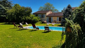 Une maison avec une piscine, entourée de pelouse et d’arbres.