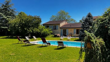 Une maison avec une piscine, entourée de pelouse et d’arbres.
