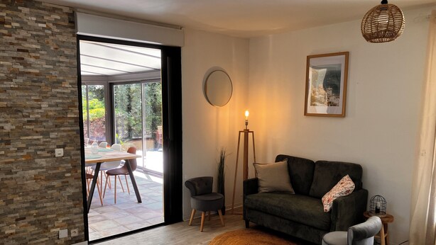 Un salon moderne avec un canapé, des fauteuils, un lampadaire et un coin repas visible à travers une porte vitrée.