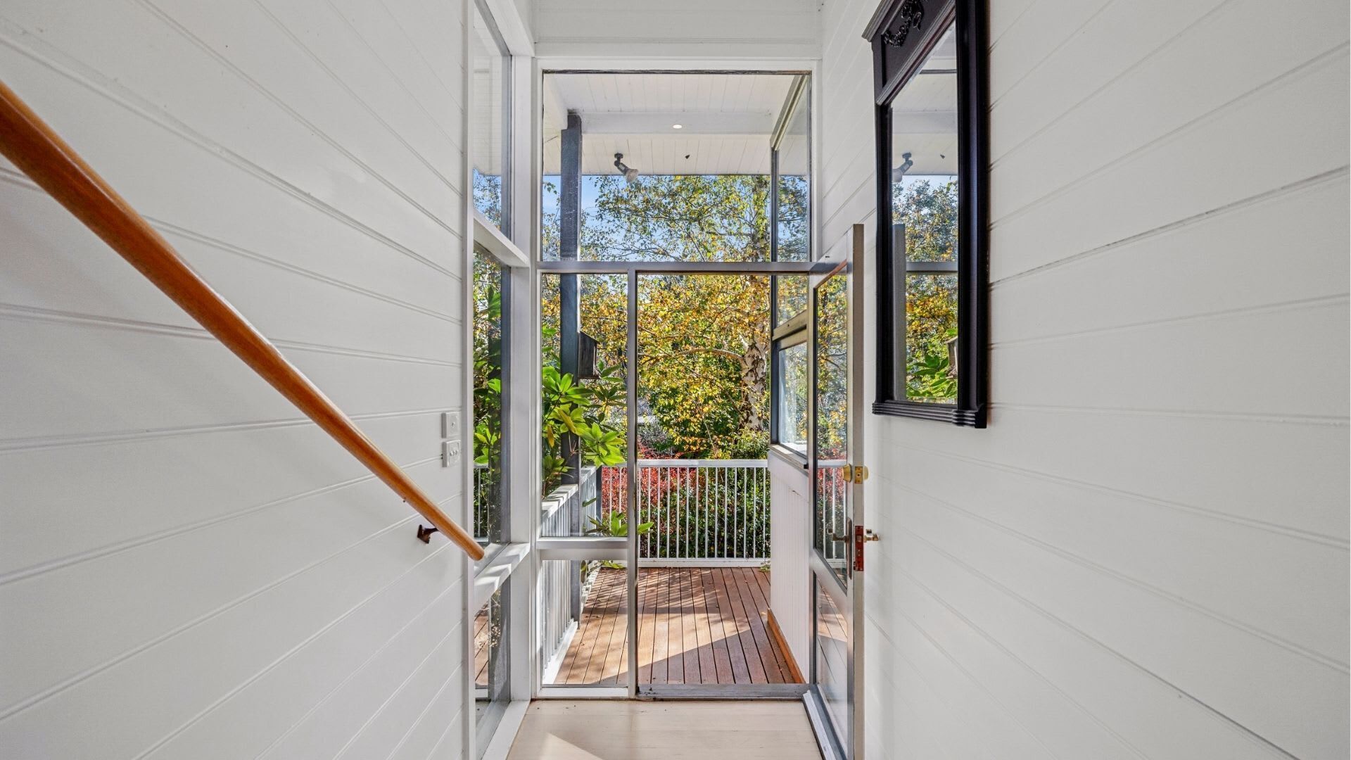 Un intérieur moderne avec un escalier en bois menant à un balcon d’où l’on peut admirer la vue sur les arbres.