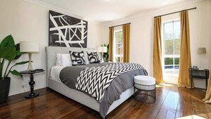 Een moderne slaapkamer met een groot bed, een nachtkastje, een potplant en een raam met gordijnen.
