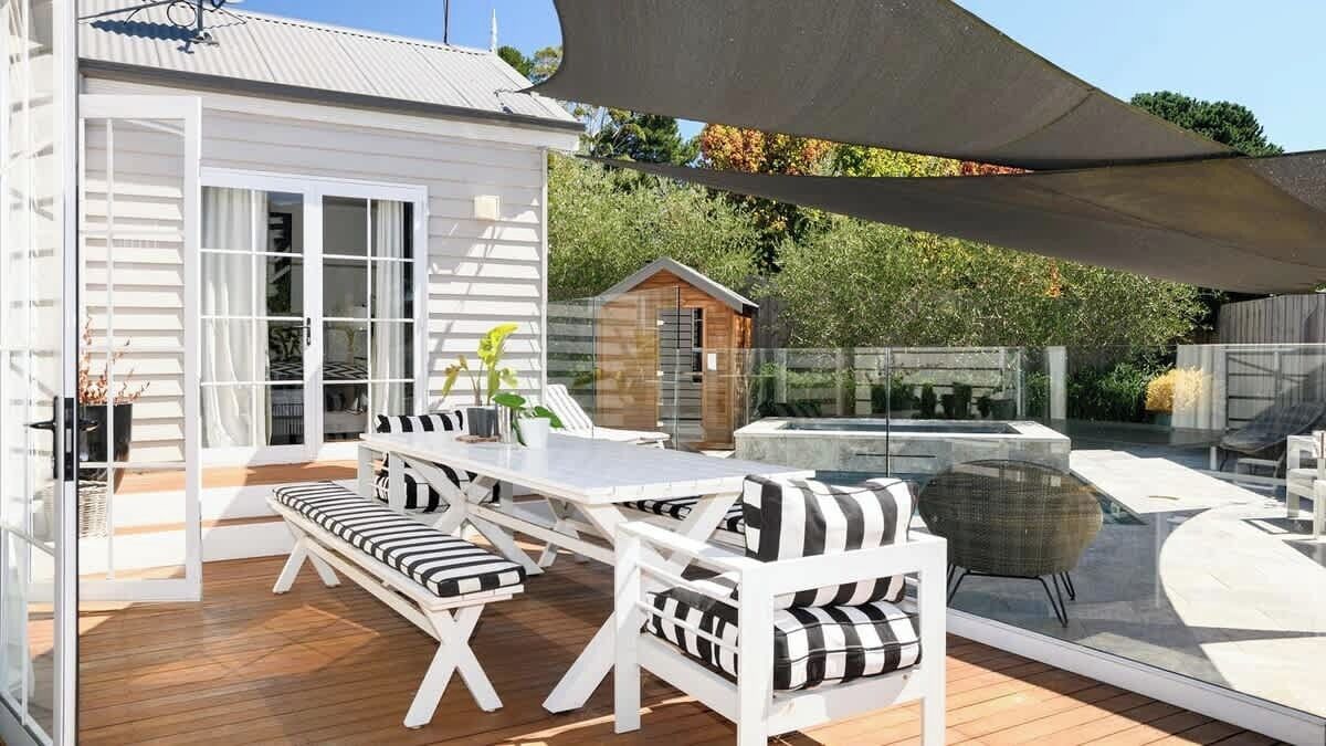 A patio with a table and chairs, a small wooden structure, and a glass enclosure.