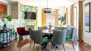Een eetgedeelte met een ronde tafel, groene bekleden stoelen en een rode stoel.