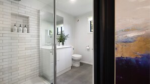 A modern bathroom with white tiles, a glass shower enclosure, a toilet, and a sink with toiletries. - Emerson Retreat Daylesford (Daylesford)