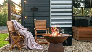 Ein Außenbereich mit Sitzgelegenheit, zwei Holzstühlen, einem Feuerkorb und einem Grill.