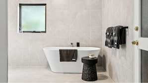 A modern bathroom with a freestanding bathtub, a small round stool, and a towel rack with multiple towels.