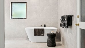 Un baño moderno con una bañera independiente, un taburete redondo pequeño y un perchero con varias toallas.