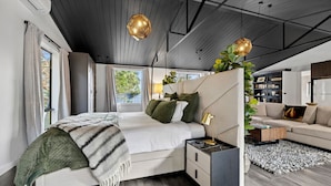A modern bedroom with a large bed, bedside tables, a sofa, and a view of the outdoors.