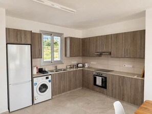 Eine moderne Küche mit Holzausstattung, einer integrierten Waschmaschine, einem Herd und einem Fenster mit Blick auf Grünflächen.