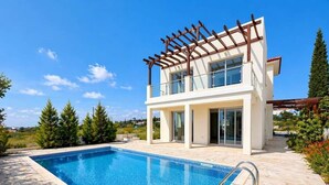 Ett modernt hus i två våningar med en swimmingpool, en pergola och utsikt över det omgivande landskapet.