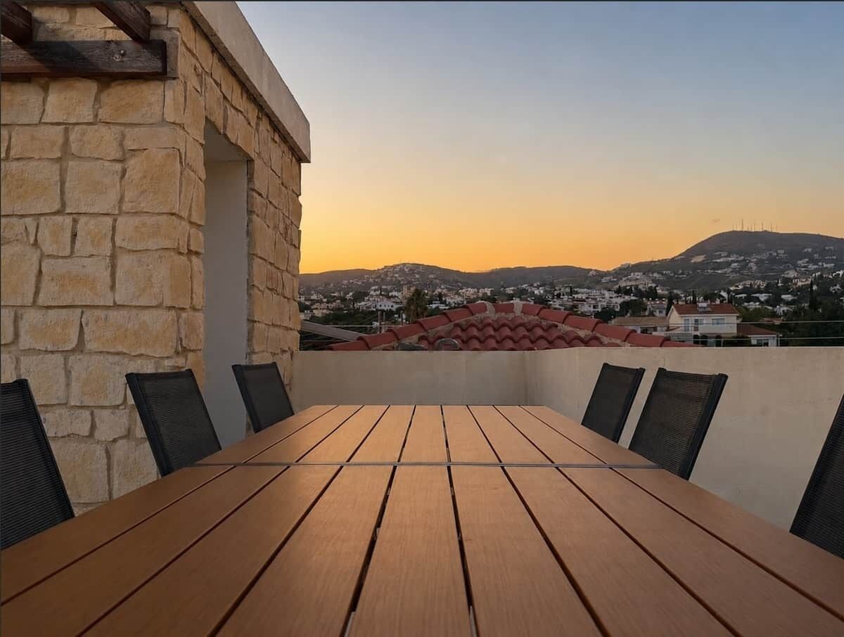 A wooden table with chairs on a balcony overlooking a cityscape with mountains.