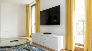 A modern room with a TV mounted on the wall, a glass table with a remote, and a white cabinet. - Modern 1-Bedroom Greenwich Apartment - Close to O2 Arena (London)