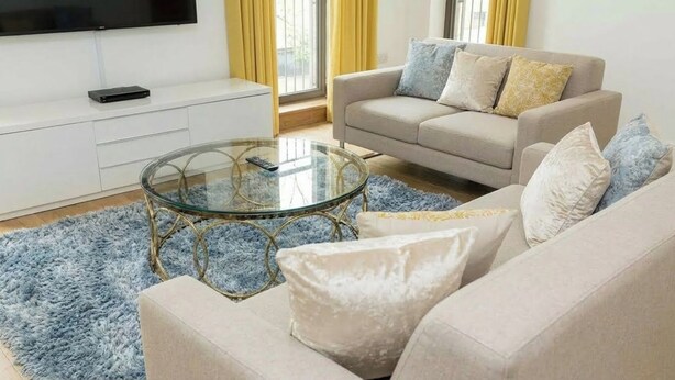 A living room with a sofa, a glass coffee table, a flat-screen TV, and a white cabinet. - Modern 1-Bedroom Greenwich Apartment - Close to O2 Arena (London)
