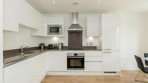 A modern kitchen with white cabinetry, a stainless steel range hood, a built-in oven, and a microwave. - Modern 1-Bedroom Greenwich Apartment - Close to O2 Arena (London)