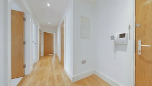 A hallway with wooden flooring, white walls, and doors on both sides. - Modern 1-Bedroom Greenwich Apartment - Close to O2 Arena (London)