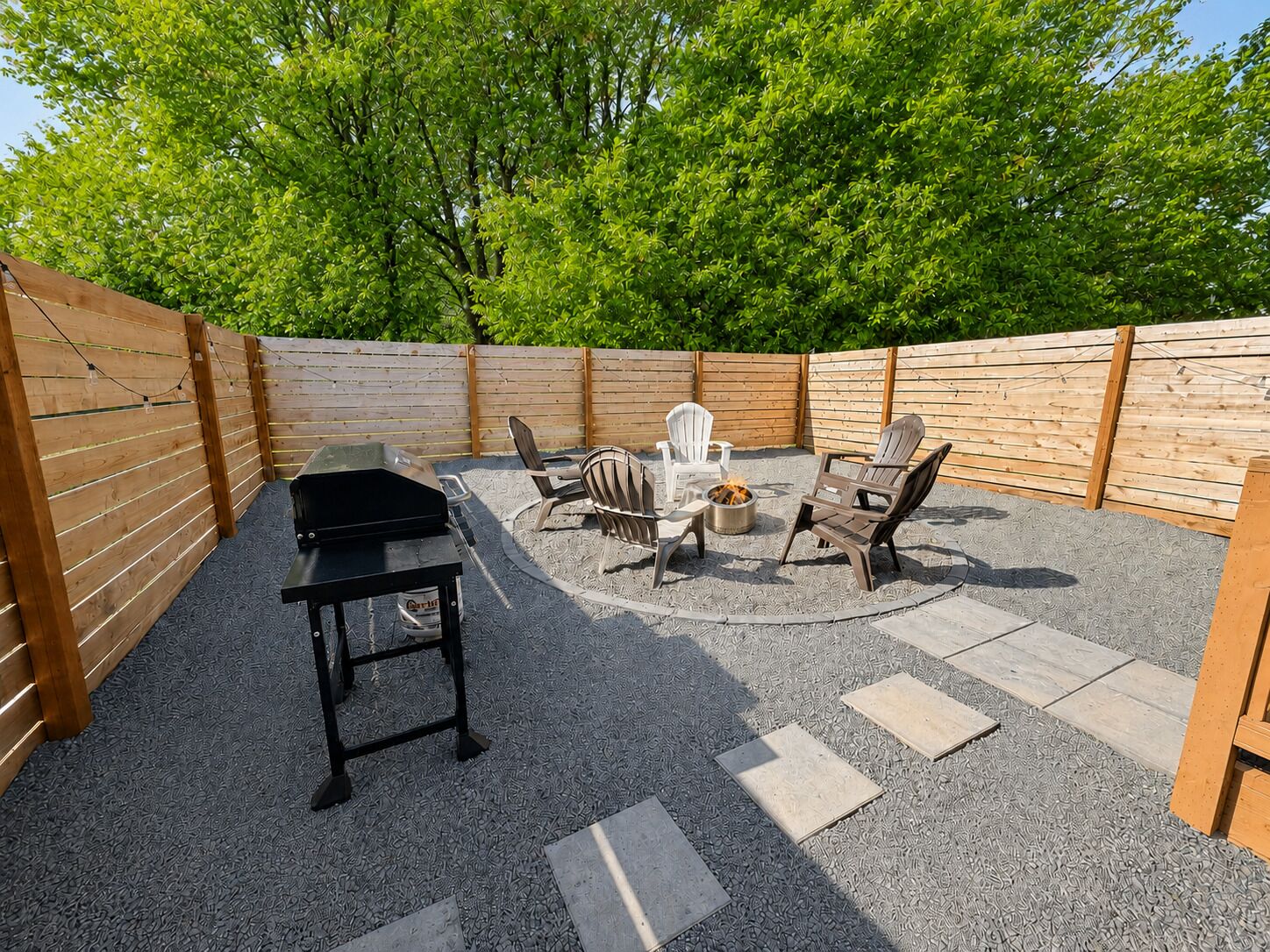 Une terrasse à l’arrière de la maison, équipée d’un barbecue, de meubles d’extérieur et d’un foyer.