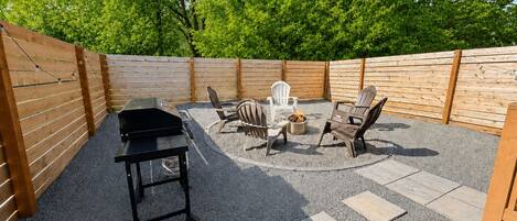 Une terrasse à l’arrière de la maison, équipée d’un barbecue, de meubles d’extérieur et d’un foyer.