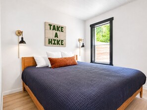 Une chambre à coucher avec un lit, une fenêtre, un panneau fixé au mur et deux lampes murales.