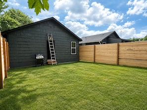A backyard with a wooden fence, a grill, and a ladder leaning against a shed.