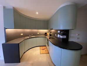 A modern kitchen with curved cabinetry, a built-in sink, and a coffee machine. - Luxury Sea View Retreat in Groenendijk (Koksijde)