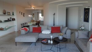 Ein modernes Wohnzimmer mit einem grauen Sofa, roten Kissen, einem Couchtisch und einem Essbereich im Hintergrund.