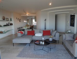 A modern living room with a grey sofa, red cushions, a coffee table, and a dining area in the background. - Luxury Sea View Retreat in Groenendijk (Koksijde)