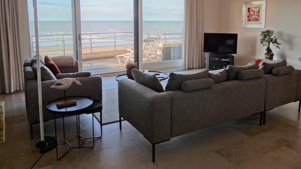Ein Wohnzimmer mit Sofa, Fernseher und Blick auf den Strand.