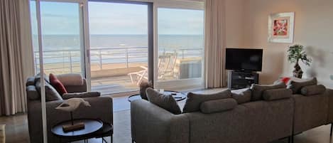 Una sala de estar con sofá, televisor y vista a la playa.
