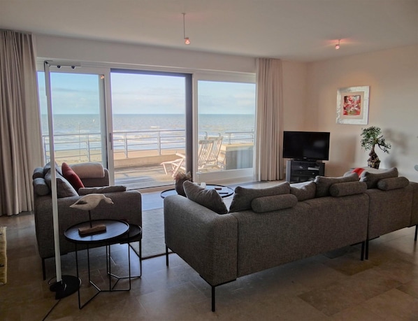 A living room with a sofa, a TV, and a view of the beach. - Luxury Sea View Retreat in Groenendijk (Koksijde)