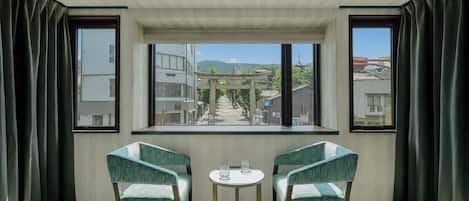 Una habitación con dos sillas, una mesita y vistas a un paisaje urbano a través de amplios ventanales.