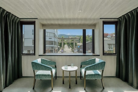 A room with two chairs, a small table, and a view of a cityscape through large windows.