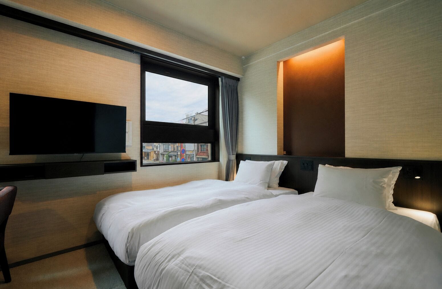 Une chambre d’hôtel avec deux lits, un téléviseur à écran plat fixé au mur et une fenêtre donnant sur la ville.