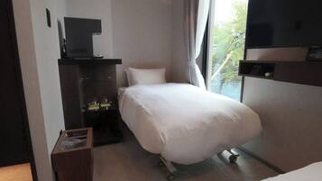 A hotel room with a bed, a television, a desk with a computer, and a window with a view of trees.