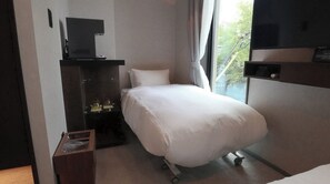 Una habitación de hotel con cama, televisión, escritorio con computadora y ventana con vista a árboles.