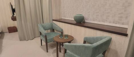 Een kamer met een ronde tafel en twee stoelen, een vaas op een plank, en een gordijn.