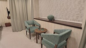Una habitación con una mesa redonda y dos sillas, un florero en una repisa, y una cortina.
