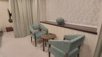 Um quarto com uma mesa redonda e duas cadeiras, um vaso numa estante e uma cortina.