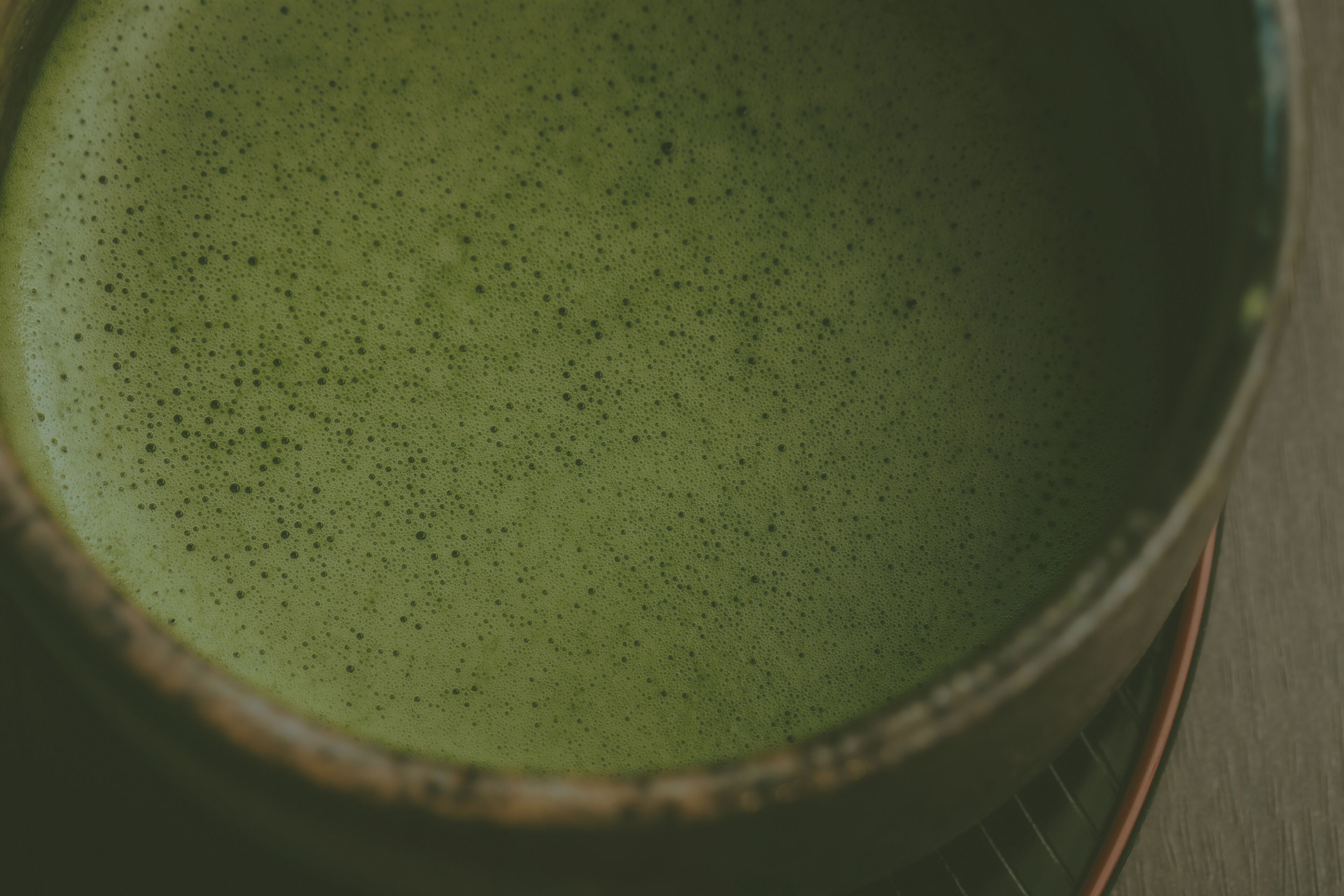 Gros plan d’une tasse en céramique contenant un liquide vert, vraisemblablement du thé ou du café, posée sur une surface en bois.