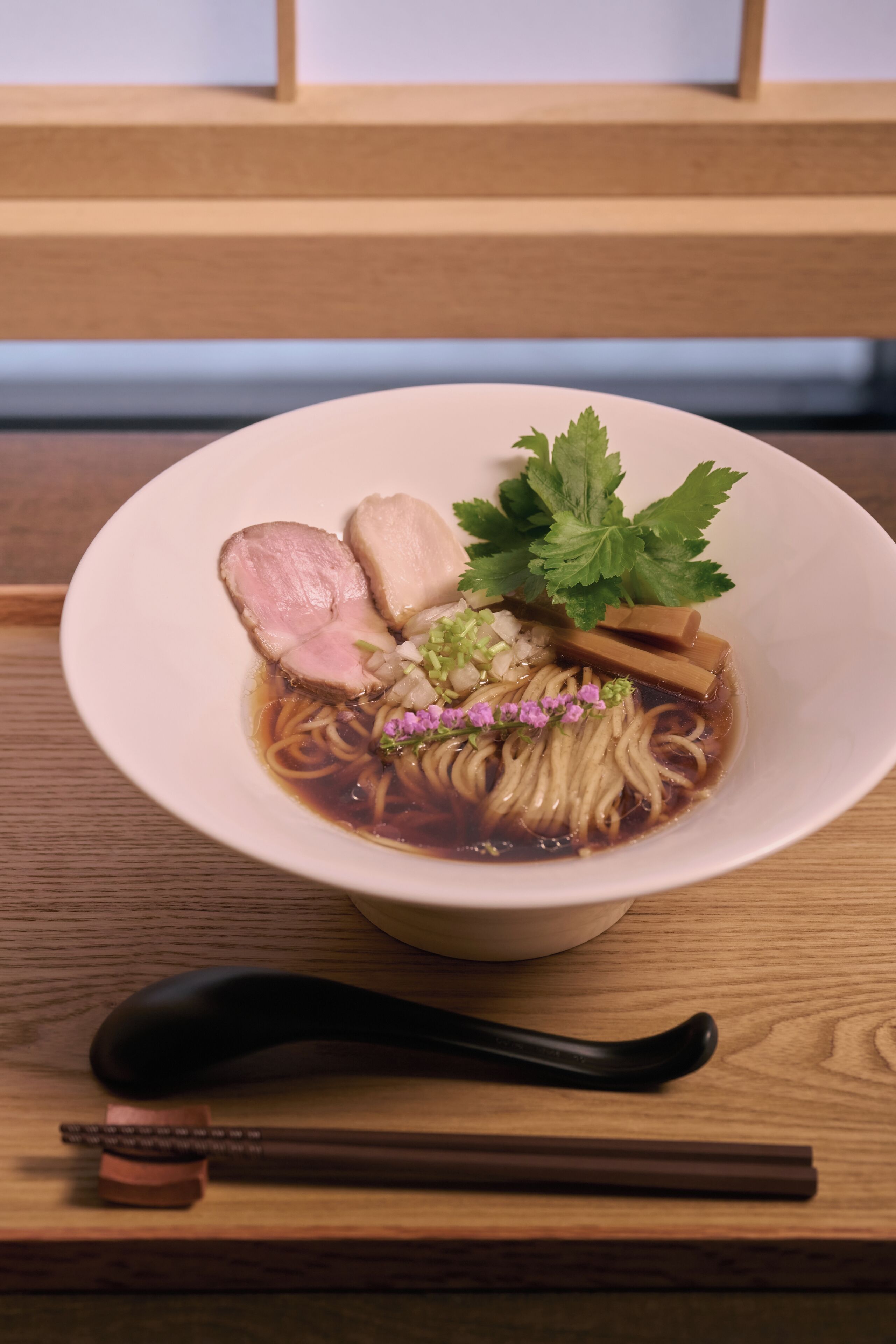 Een kom ramen met diverse toppings op een houten tafel.