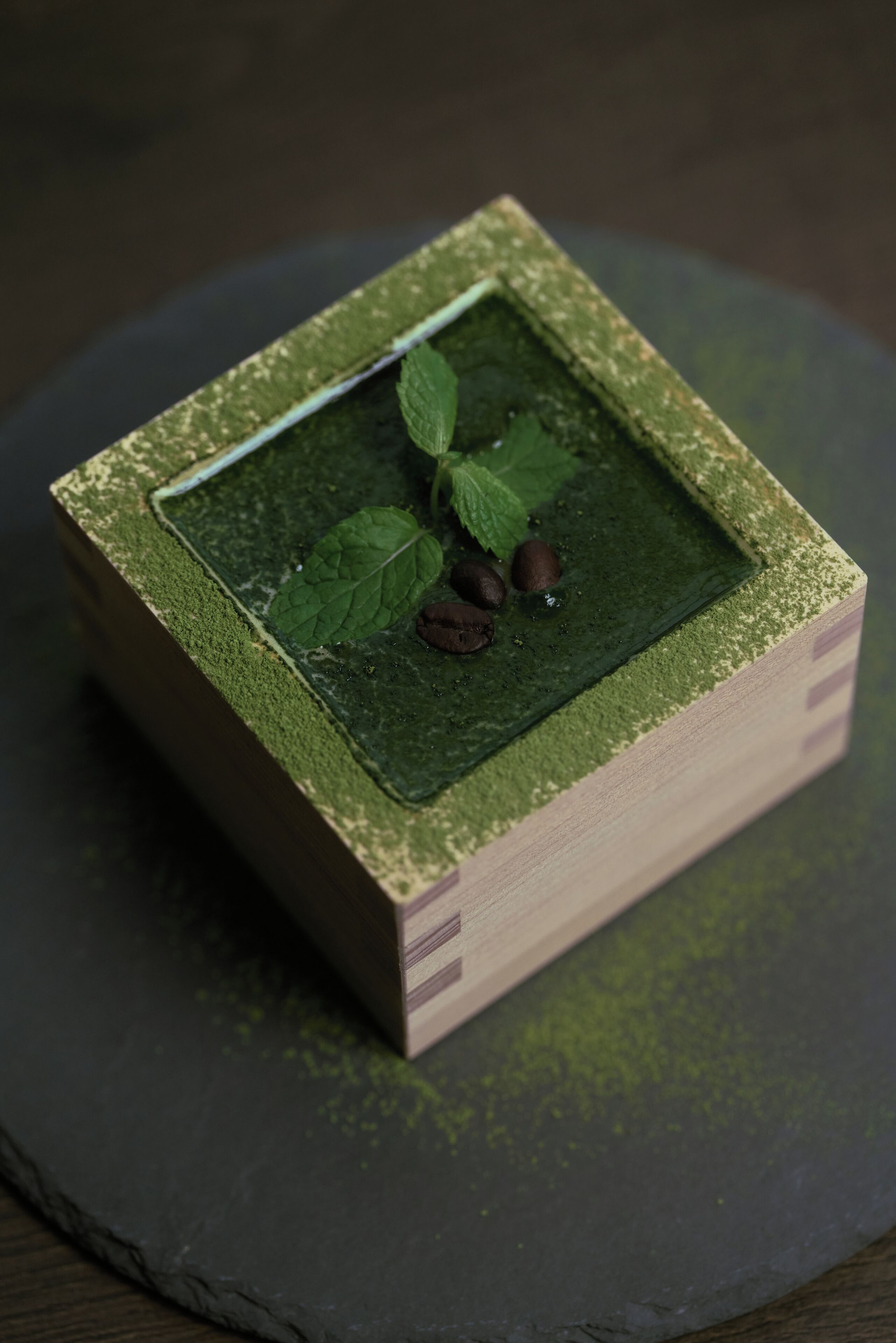 Un objet de forme carrée, doté d’une surface texturée, qui pourrait être une boîte ou un récipient, placé sur une surface sombre.