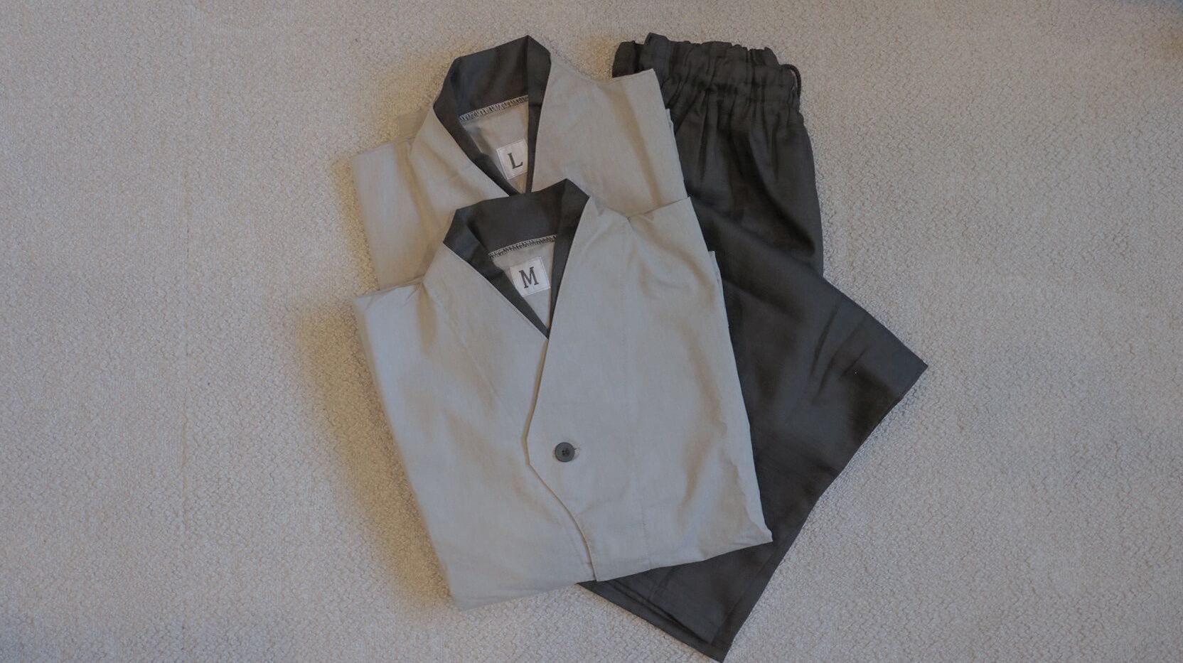 A neatly folded pair of formal attire, including a white shirt and black trousers, on a textured carpet.
