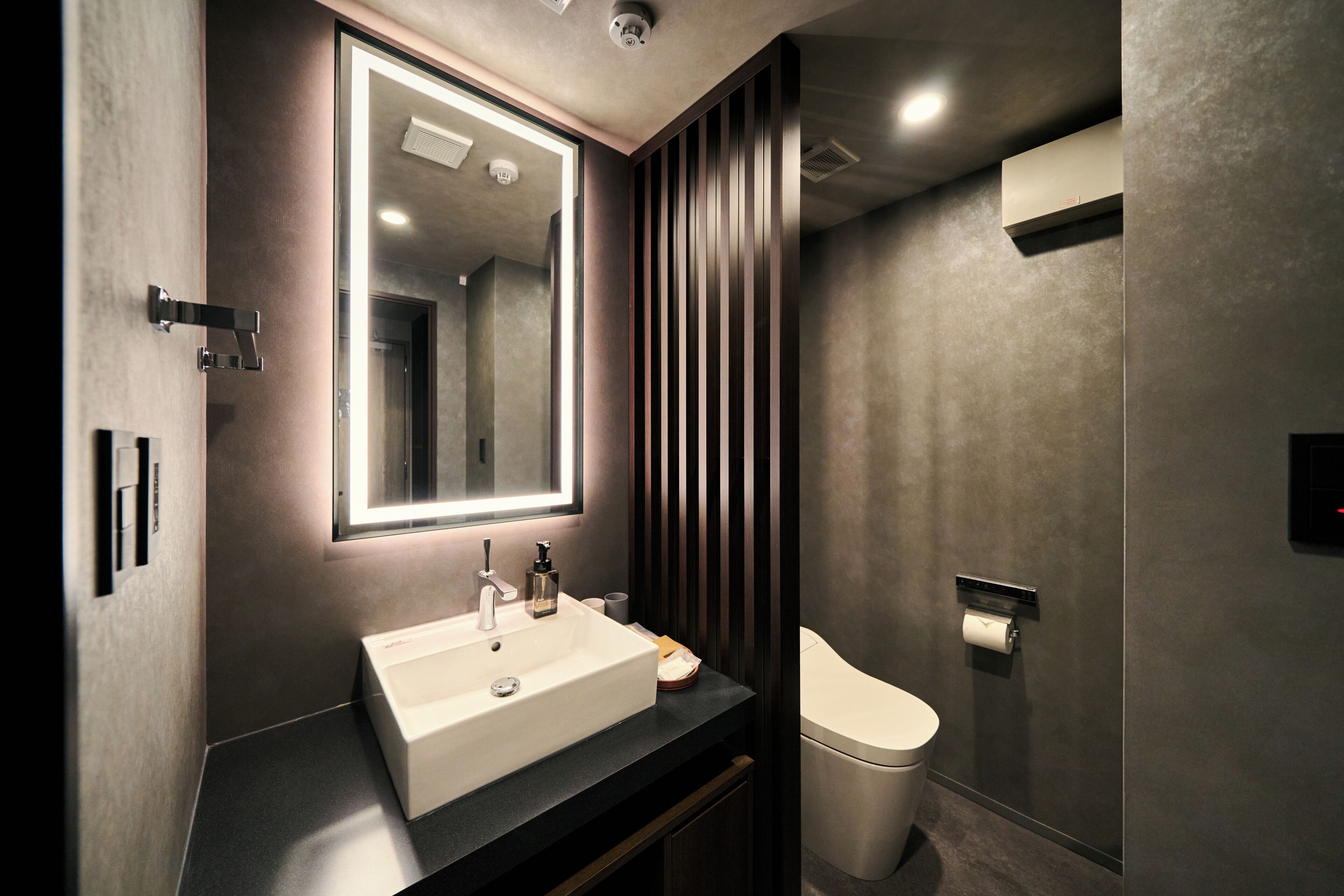 Une salle de bain moderne avec un grand miroir, un lavabo, des toilettes et un espace douche.
