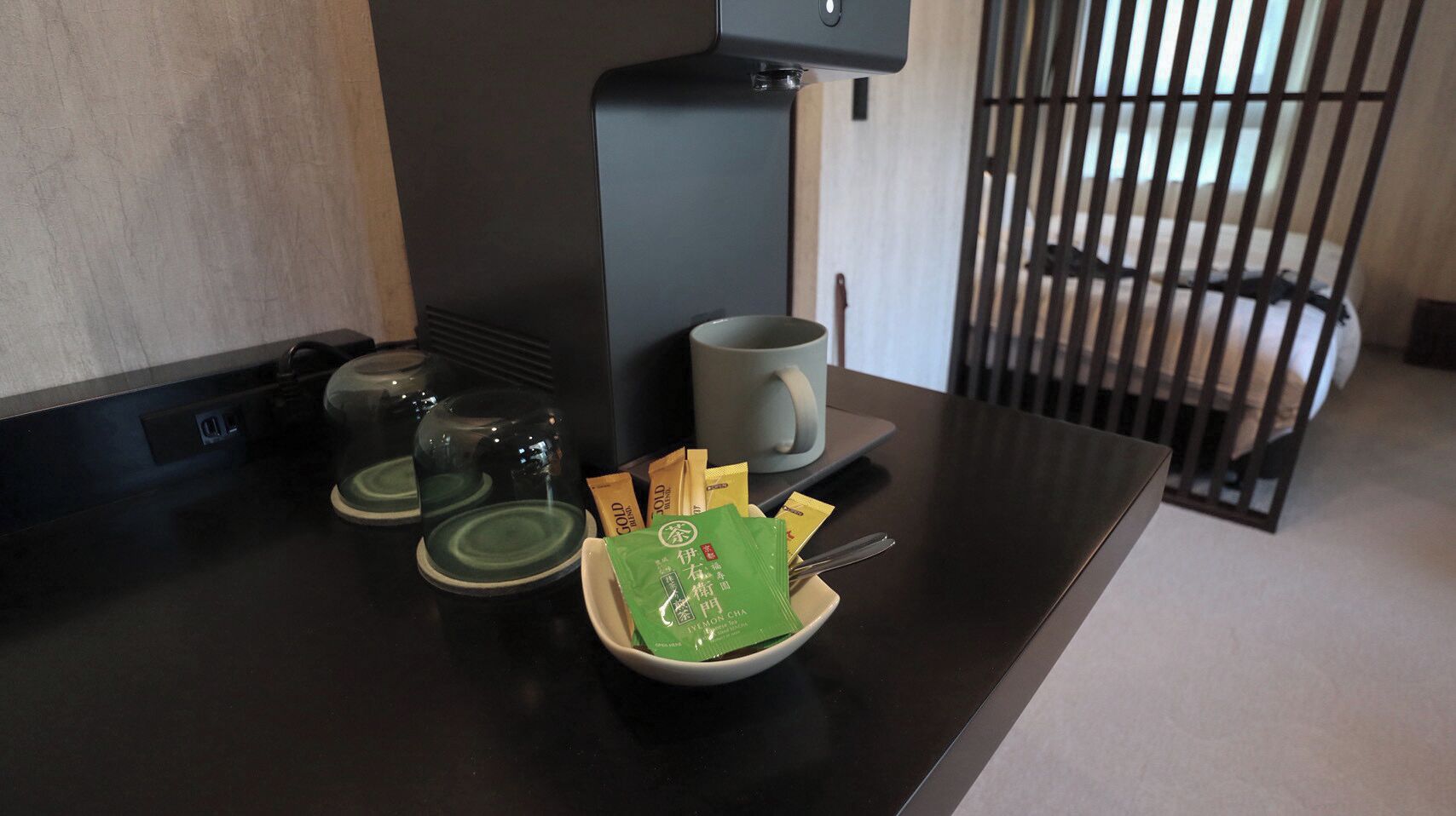 A coffee station with a coffee machine, cups, and a bowl of coffee packets.