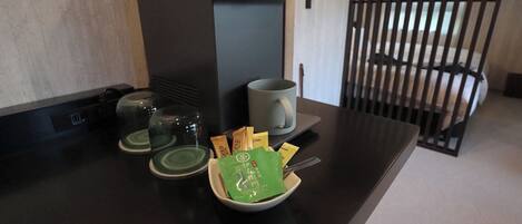 A coffee station with a coffee machine, cups, and a bowl of coffee packets.